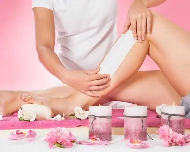 Waxing procedure with candles and flowers on a pink background.