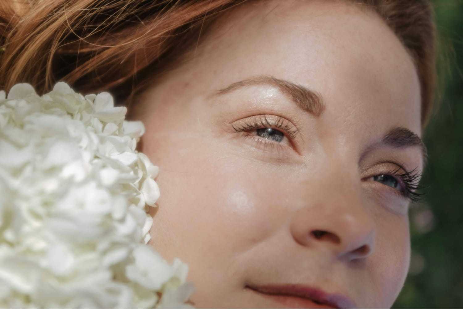 Close-up of a woman's serene face next to white hydrangea flowers.