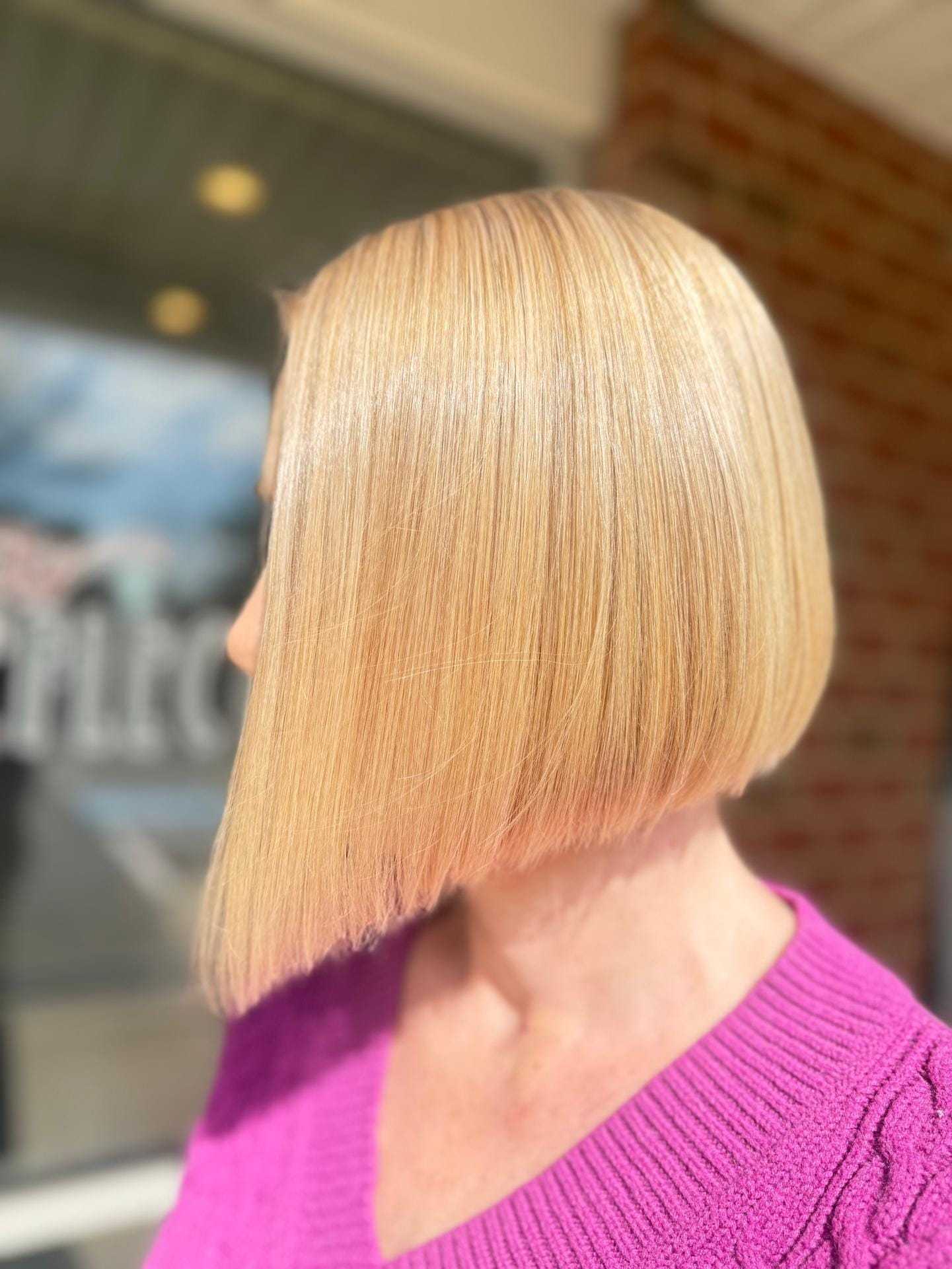 Woman with sleek bob haircut in bright pink sweater, showcasing smooth, shiny blonde hair.