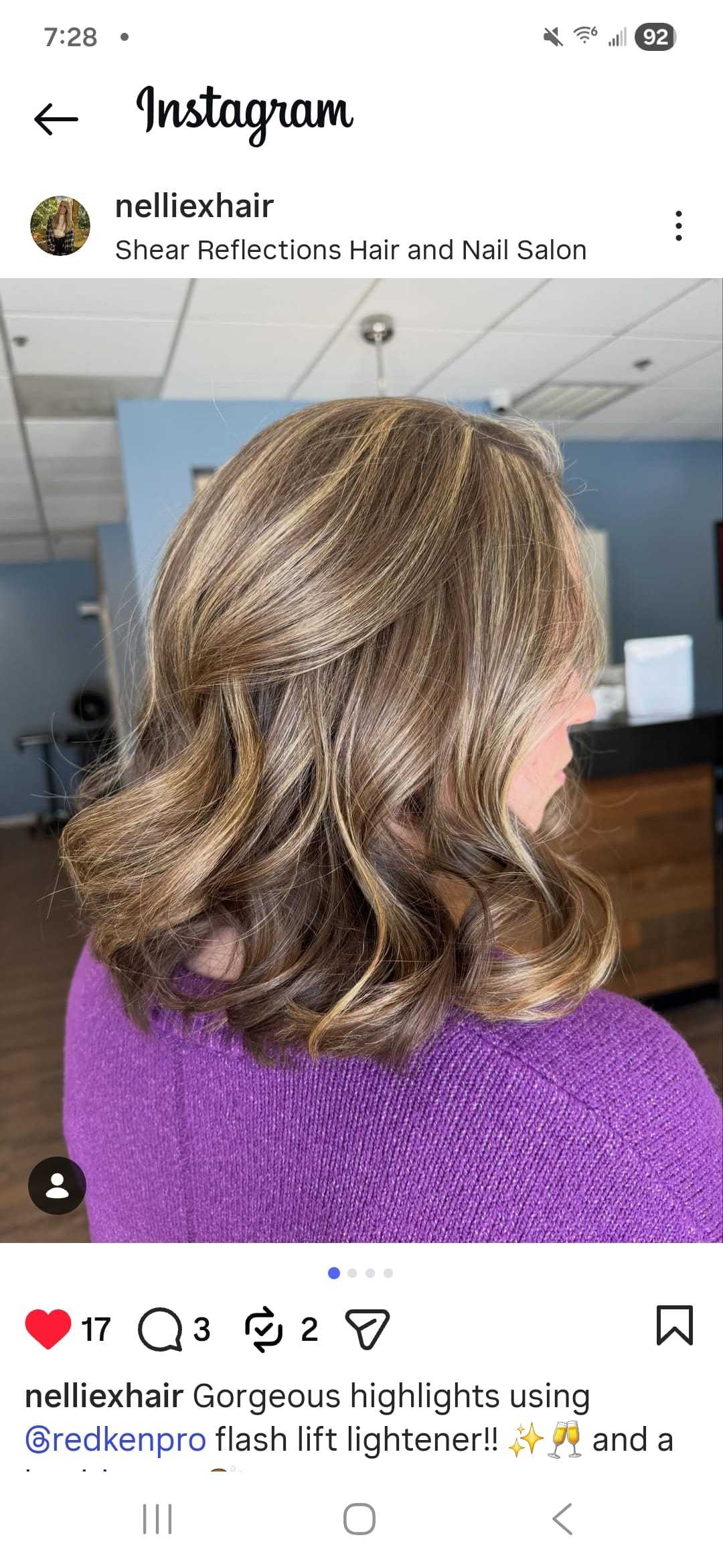 Woman with highlighted hair, styled in loose waves, inside a salon in a purple sweater.